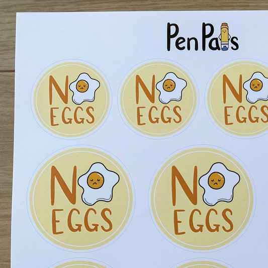 A sheet of round stickers printed with the phrase 'NO EGGS' and a cartoon fried egg, branded 'PenPal's' at the top, shown on a light wood surface.