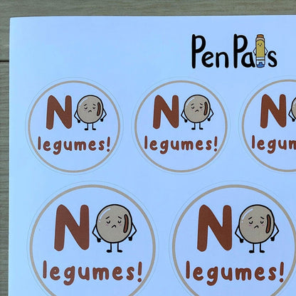 A sheet of circular labels printed with the text 'NO legumes!' and a cartoon potato character, shown on a light wood surface. The brand name 'PenPals' appears at the top.